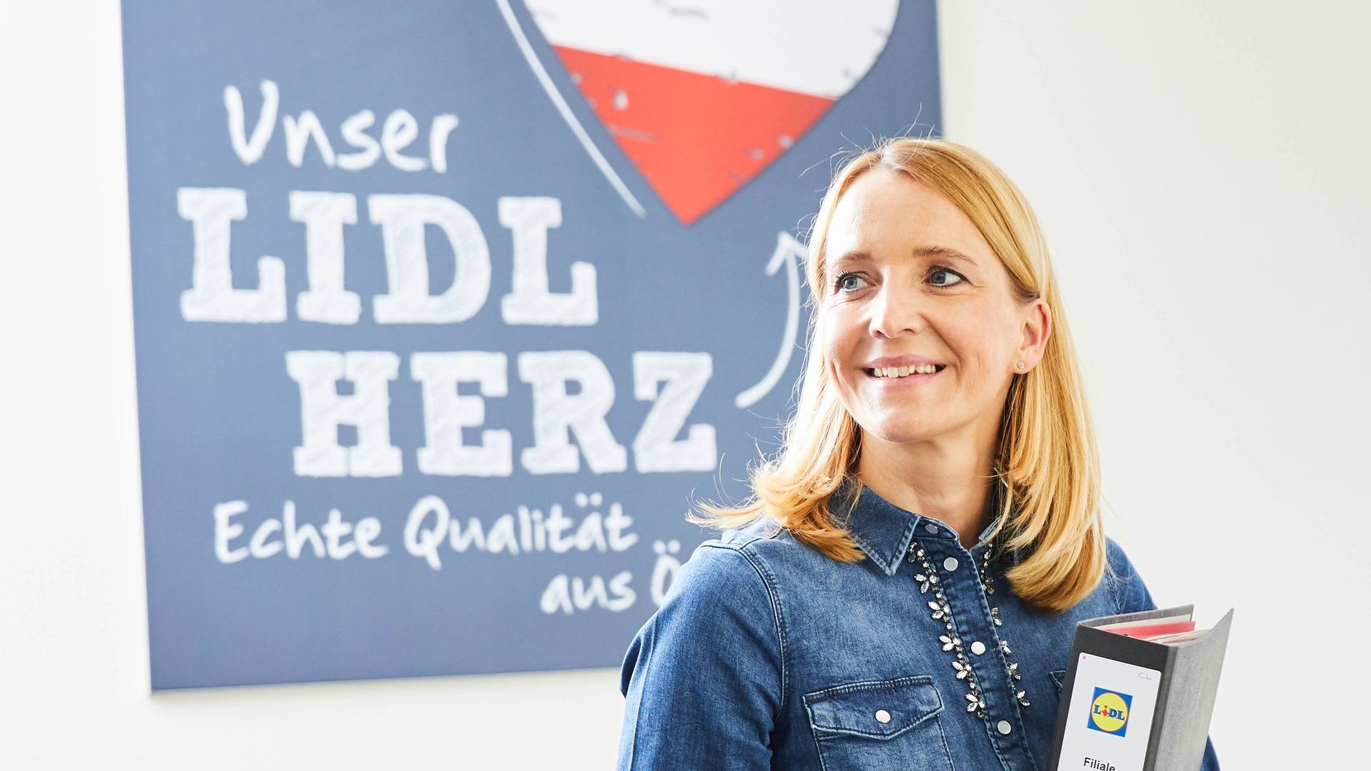 Eine Mitarbeiterin steht mit einem Ordner in einem Gang.